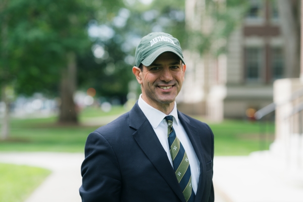Scott Brown, a light-skinned, clean-shaven man wearing a green Dartmouth baseball cap and a suit and tie.